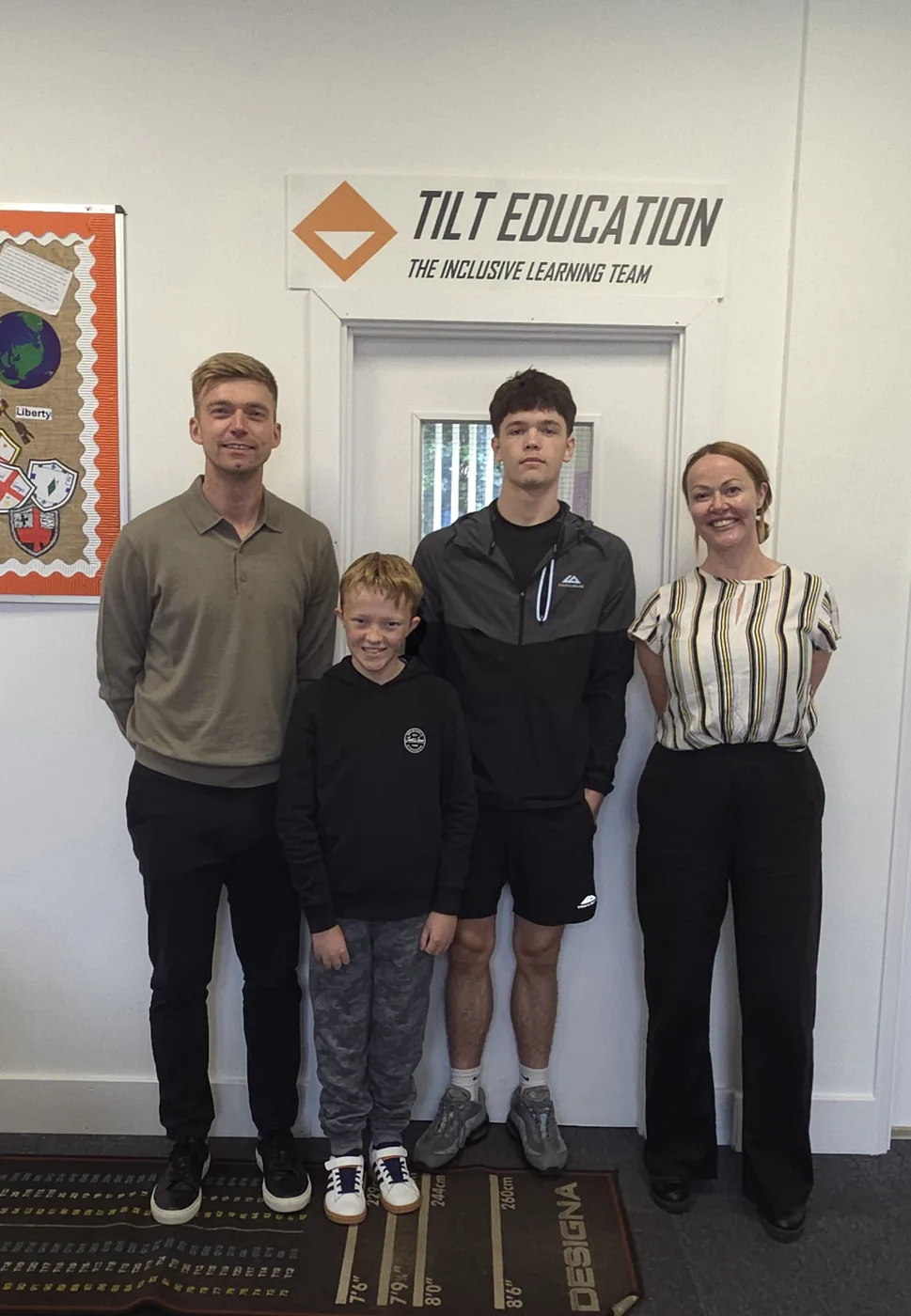 Two adults and two pupils standing under a TILT Education sign in a school corridor